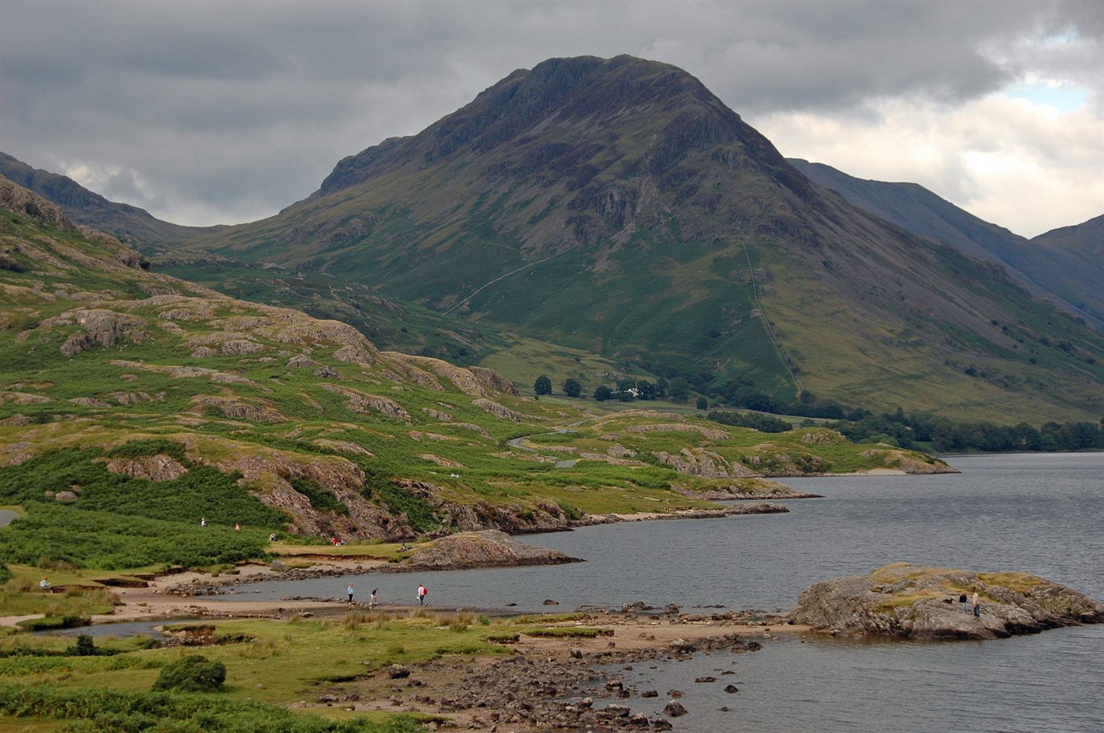 A lake shore below a green fell under cloudy skies in the English Lake District